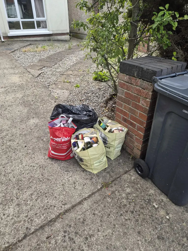 A supermarket bag of glass bottles next to a household wheelie bin, showing where glass should not go.
